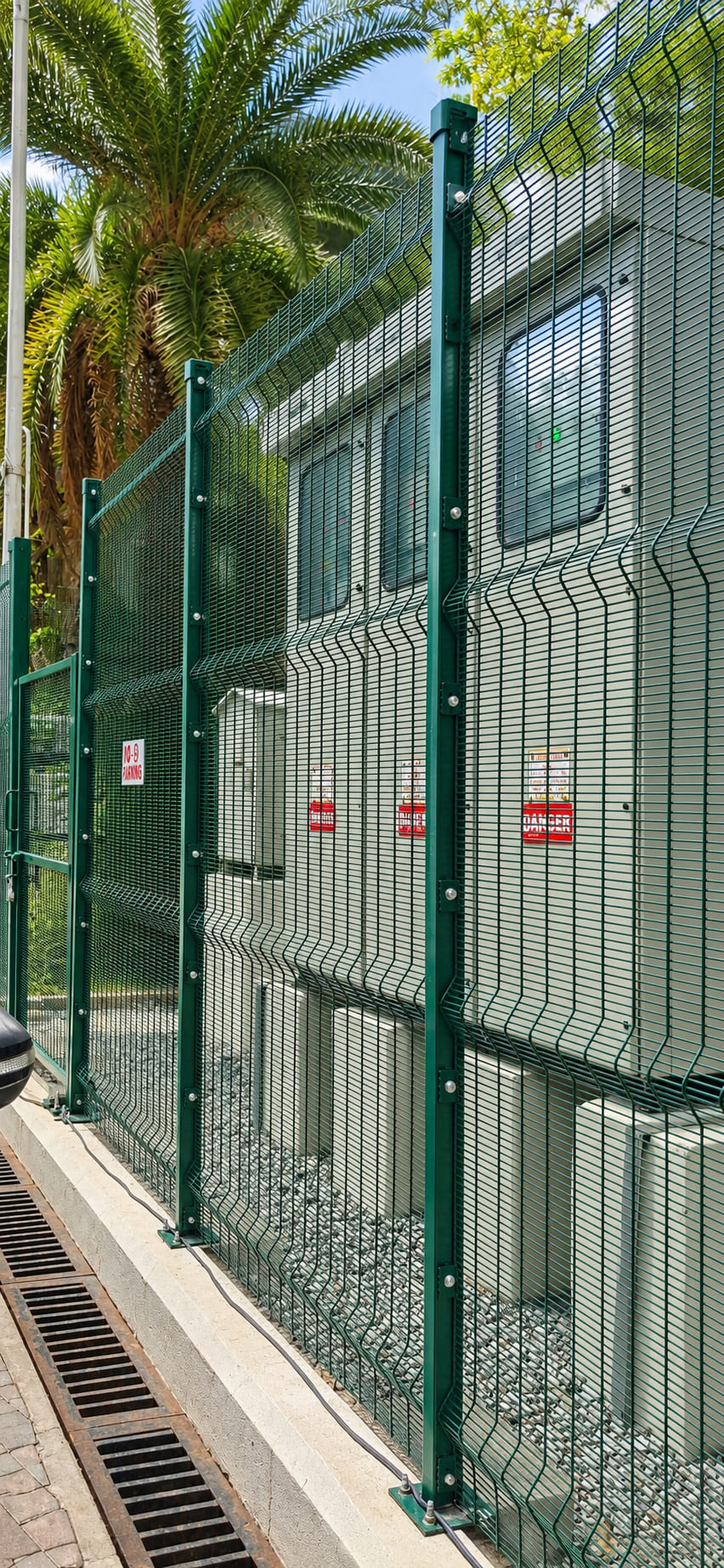 Green powder-coated 3D welded mesh security fence installed around electrical equipment for industrial perimeter protection.