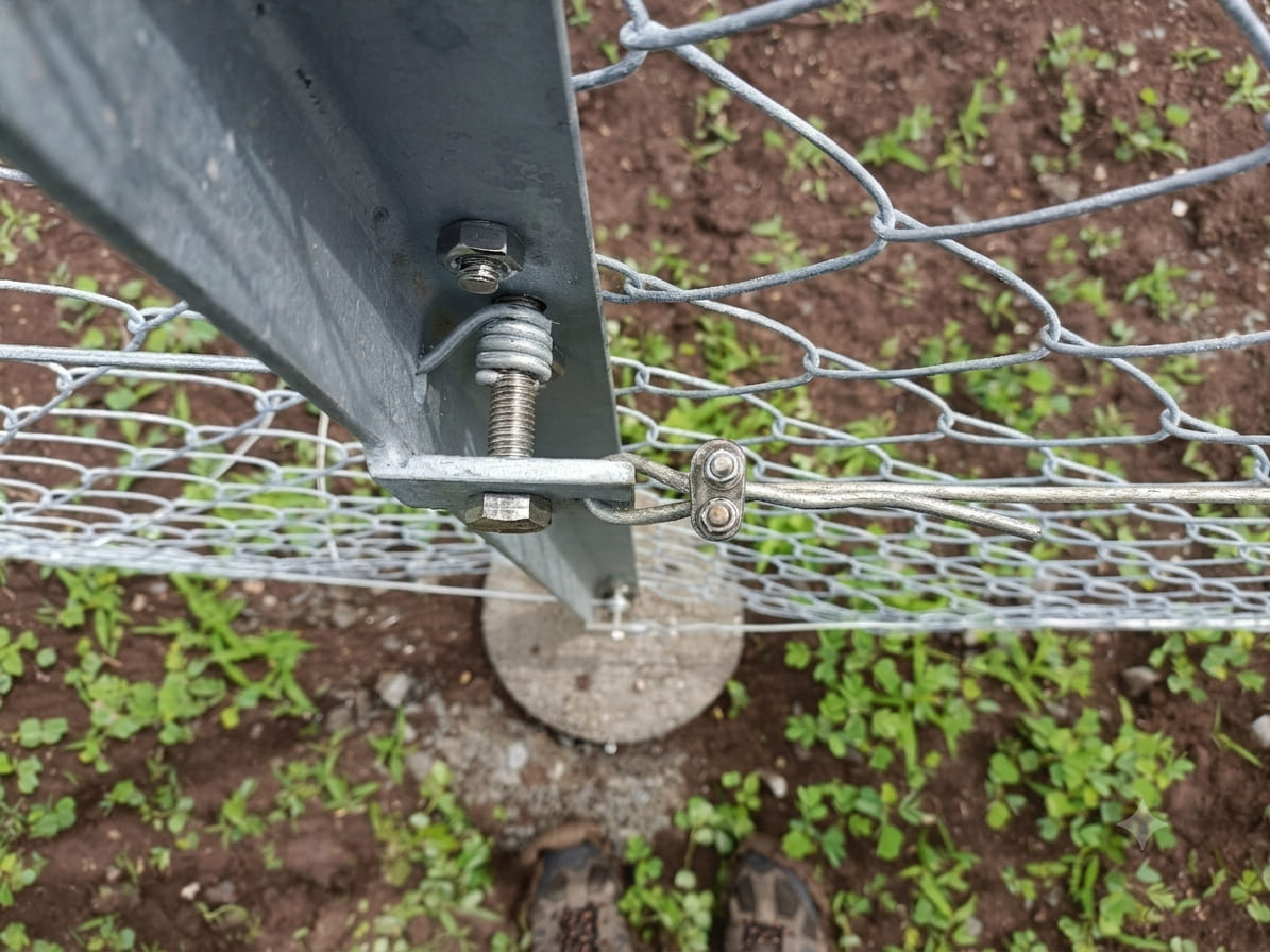 Close-up of a galvanized chain link fence tension wire system with adjustable tensioning hardware installed on a galvanized steel angle post.