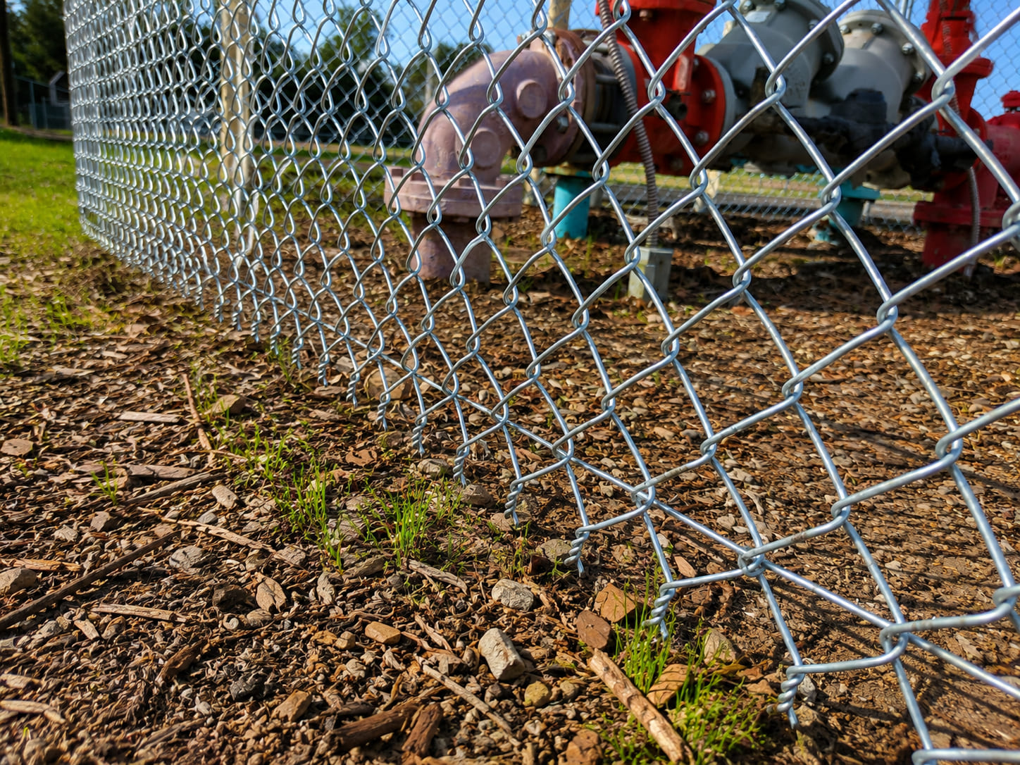 Close-up of a galvanized chain link fence showing the knuckled bottom selvage for industrial perimeter and utility security fencing.