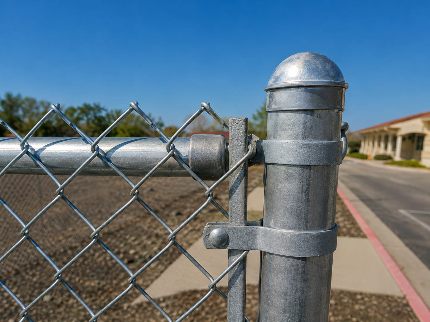 Close-up of a galvanized chain link fence terminal post with post cap, top rail, and heavy-duty galvanized hardware.
