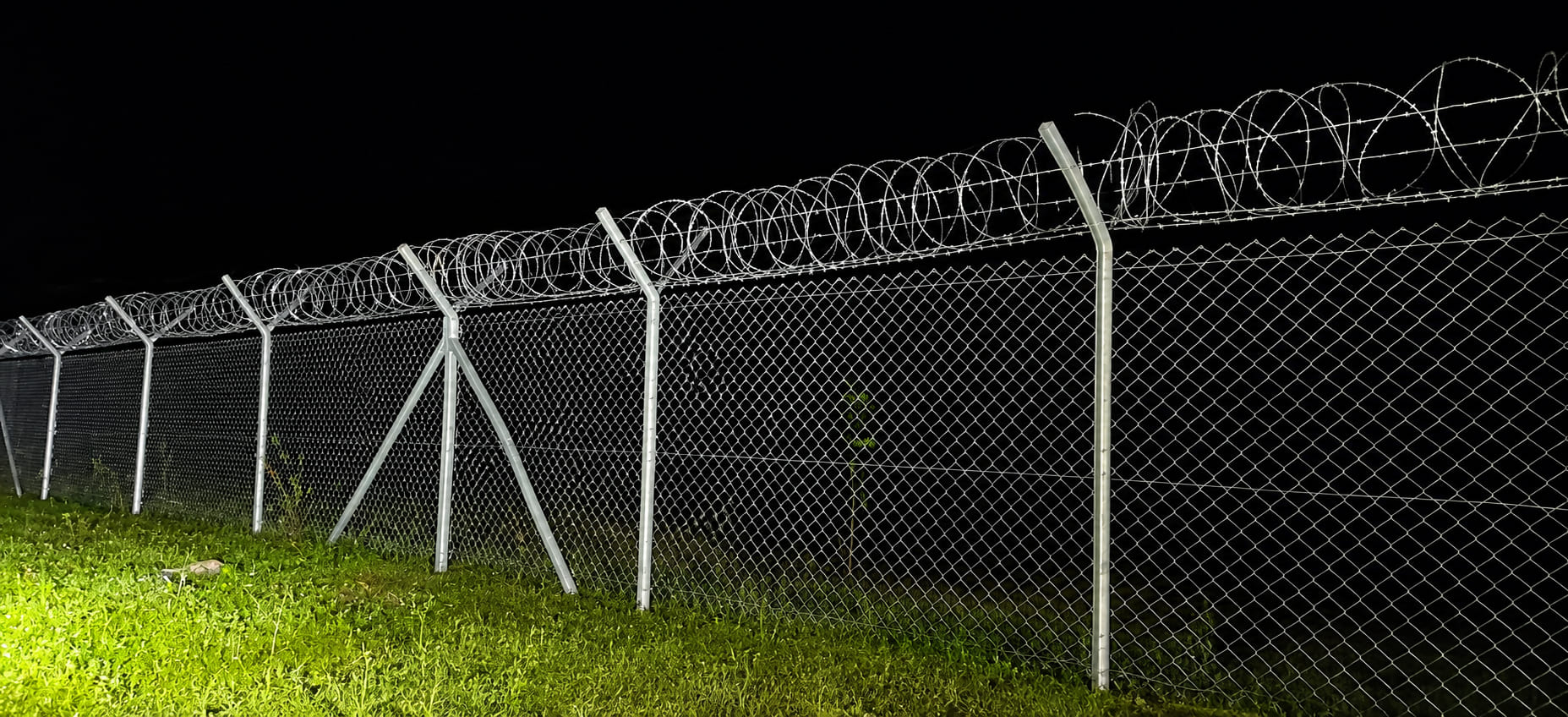 Night view of a galvanized chain link fence topped with concertina coil for high-security industrial perimeter protection.