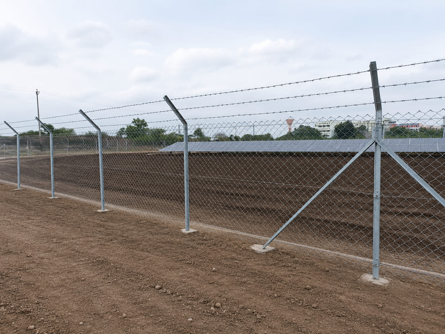 Galvanized chain link fence with three-strand barbed wire installed for solar power plant perimeter security and site protection.